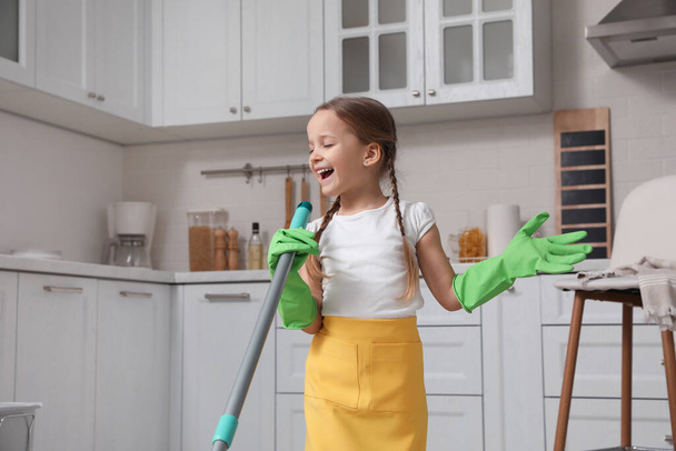 Cute little girl with mop singing while cleaning at home - Foto, Imagen