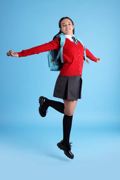 Teenage girl in school uniform with backpack jumping on light blue background - Φωτογραφία, εικόνα