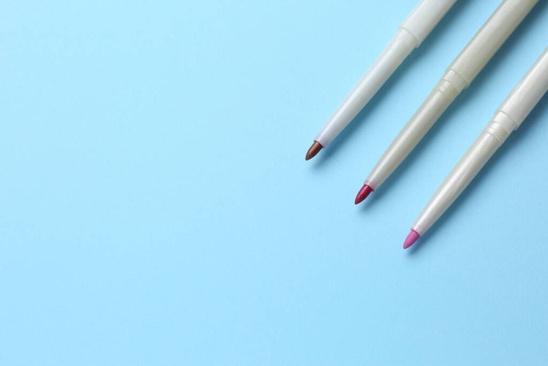 Different lip pencils on light blue background, flat lay with space for text. Cosmetic product - Foto, imagen