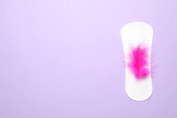 Sanitary pad with pink feather on violet background, top view and space for text. Menstrual cycle - Photo, Image