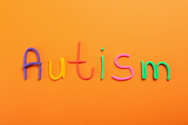 Word Autism made with colorful plasticine on orange background, flat lay - 写真・画像