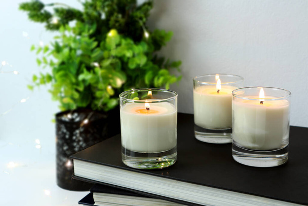 Luxus-Beleuchtung aromatische Duftglaskerzen und ein paar Bücher stehen auf weißem Tisch, um romantische und entspannte Atmosphäre im weißen Schlafzimmer mit Hintergrund von kleinen Pflanzen und LED-Licht am Valentinstag zu schaffen - Foto, Bild