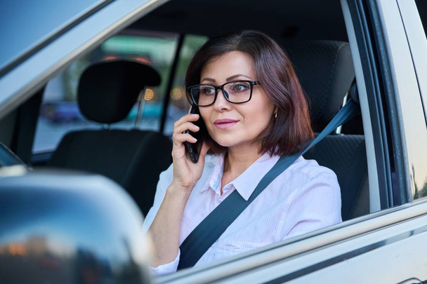 Confident female driver with smartphone driving a car - Photo, Image