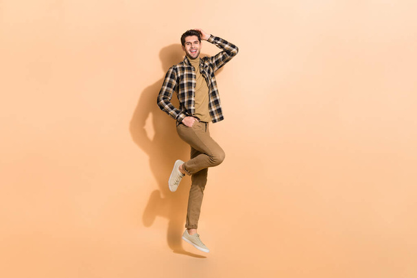 Full length body size view of attractive cheerful guy jumping posing having fun isolated on beige pastel color background - Foto, afbeelding