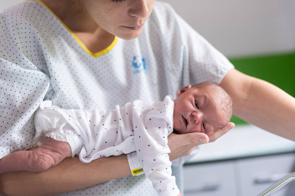 Máma, která právě porodila v nemocnici, drží své novorozeně v náručí tváří dolů, aby se zbavila plynu a zabránila kolice u kojence. novorozenec zdraví a péče - Fotografie, Obrázek