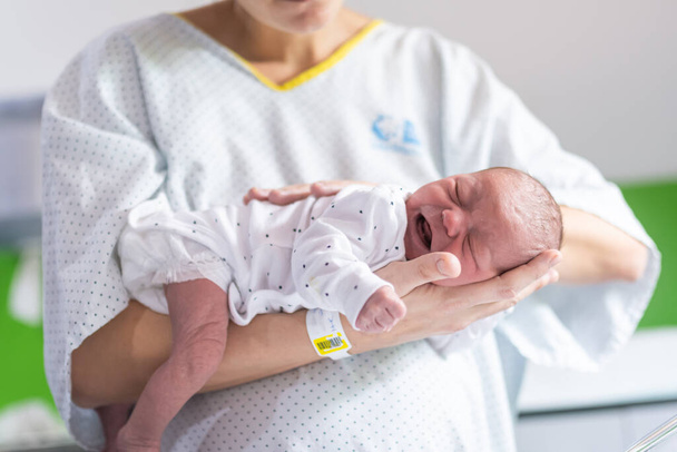 Nainen, joka on juuri synnyttänyt sairaalassa, pitää vastasyntynyttä vauvaansa käsivarsillaan rauhoittaakseen lapsen itkevää koliikkia. vastasyntyneen hoito - Valokuva, kuva