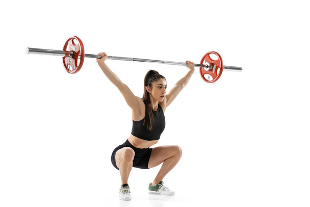 Full length portrait of muscled woman in sportswear exercising with a weight, barbell isolated on white background. Sport, weightlifting concept - Zdjęcie, obraz