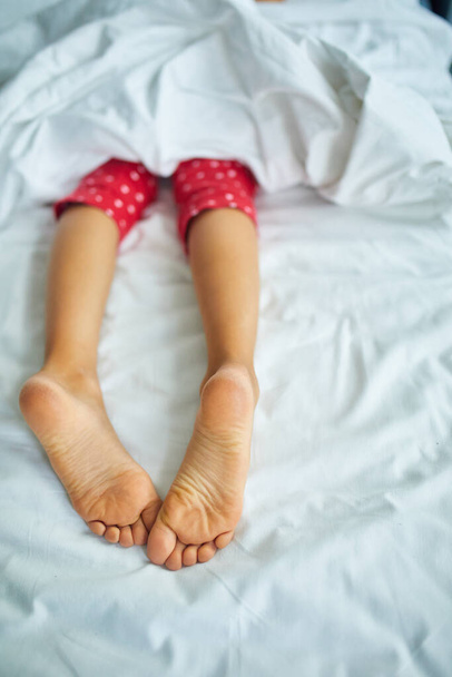 Lány lábak borított fehér ágynemű, alszik egy kényelmes ágy, Fókusz a láb, egészséges alvás a gyermekek - Fotó, kép