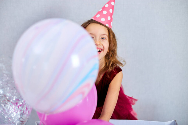 Muotokuva söpö, iloinen pieni tyttö vaaleanpunainen mekko ja hattu pelata ilmapalloja kotona syntymäpäiväjuhlat serpentiinit, Hyvää syntymäpäivää. Juhlitaan. - Valokuva, kuva