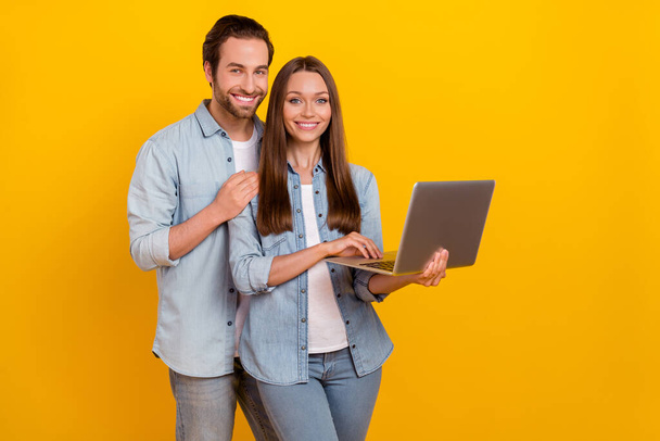 Portrait of handsome beautiful cheerful couple using laptop hugging isolated over bright yellow color background - Fotó, kép