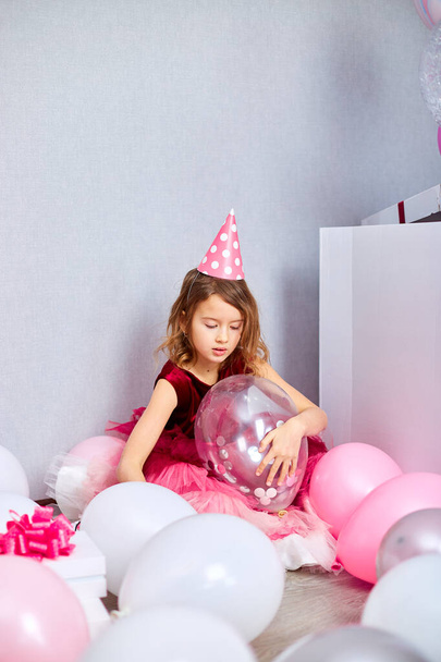 Niña en vestido rosa y sombrero de cumpleaños sentado en el suelo con muchos regalo caja, globos en casa fiesta de cumpleaños serpentinas, feliz cumpleaños. Celebrando - Foto, imagen
