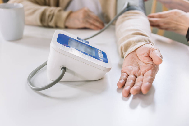 Gros plan de la main d'une femme asiatique âgée mesurant la pression artérielle à l'aide d'un tensiomètre automatique avec une infirmière. Les aidants naturels visitent les maisons. Idées de soins de santé à domicile et maisons de soins infirmiers. - Photo, image