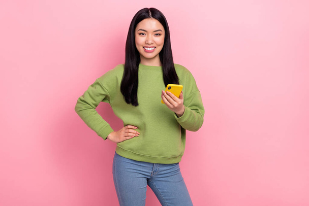 Photo of cute young lady hold telephone wear green jumper isolated on pink color background - Foto, Imagen