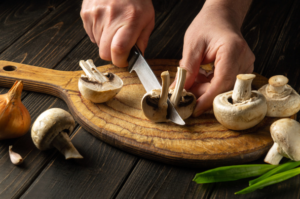 The cook cuts Agaricus mushrooms on a cutting board. Close-up of a chef hands with a knife. Vegetarian cuisine. - 写真・画像