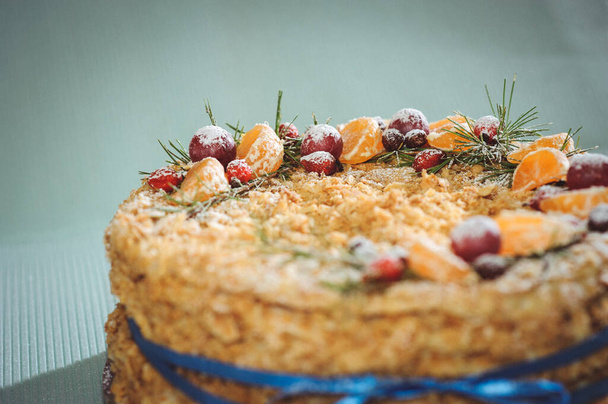 La torta di Napoleone è decorata con la composizione di anno nuovo che consiste di pezzi di mandarino, chicchi d'uva, rami di abete e brier. Una torta di foglie su sfondo blu è associata a un nastro blu - Foto, immagini