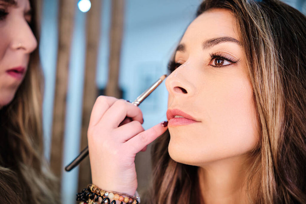Makeup καλλιτέχνης εφαρμογή eyeliner για τον πελάτη της, ενώ κάνει το μακιγιάζ της στο σαλόνι ομορφιάς. - Φωτογραφία, εικόνα