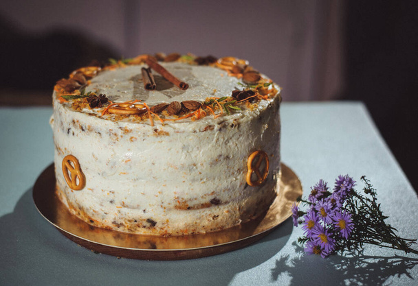 Carrot cake with nuts, prunes and dried apricots on a blue background. Purple flowers, bouquet. - Фото, зображення