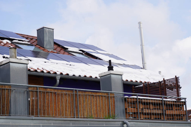 Aurinkopaneelit asuinrakennuksen katolla talvella. Ylempi moduulit ovat jo lunta, alempi moduulit ovat edelleen katettu. Pilvet kirkastuvat, taivas alkaa taas valjeta. Hieman sähköä voidaan nyt tuottaa uudelleen. - Valokuva, kuva