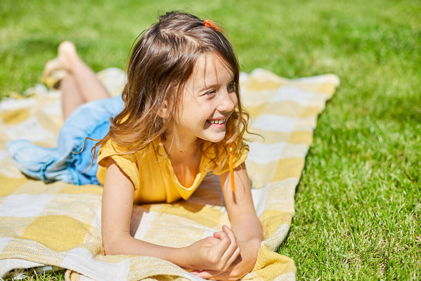 Child lying on the blanket, on the grass in the sun day, little girl take sunbathes on backyard of the house on a sunny summer day, summer time vacation. - Foto, imagen