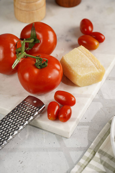 Складові для приготування: великі помідори, маленькі вишневі помідори, пармезанський сир, трава орегано, сіль і перець на мармуровій дошці
 - Фото, зображення