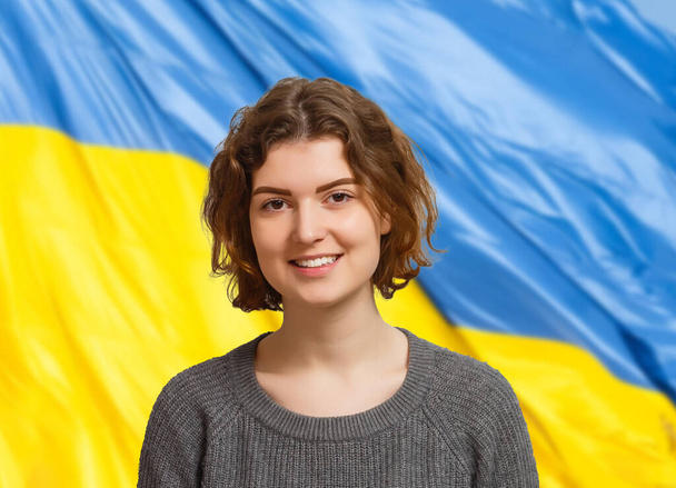 ウクライナの国旗を背景にカメラを見ている女性。ロシアとの戦争でウクライナ国民と一緒に立っての概念. - 写真・画像