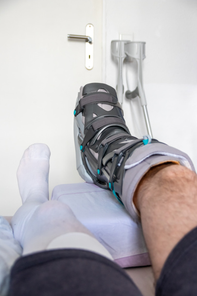 Evropan po operaci Achillovy ruptury šlach je doma se speciální fyzioterapeutickou obuví a berlemi pro zotavení doma se zdravou medicínou prášky proti bolesti nohou - Fotografie, Obrázek