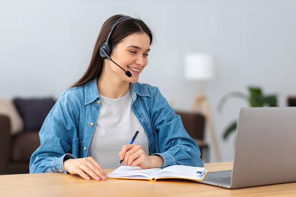 Young smiling freelancer in headset using laptop computer working online from home or modern office. Successful caucasian young female student studying, distance learning, education - Фото, зображення