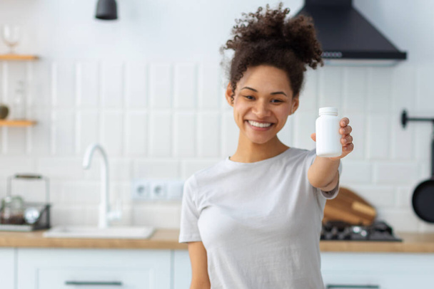 Happy young African American woman holding bottle of dietary supplements or vitamins in her hands. Close up. Healthy lifestyle concept - Φωτογραφία, εικόνα