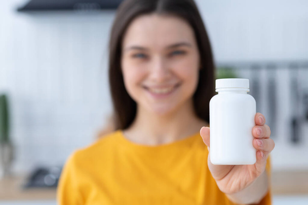 Happy young Caucasian woman holding bottle of dietary supplements or vitamins in her hands. Close up. Healthy lifestyle concept - Foto, Bild