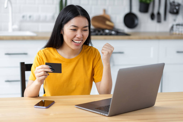 Portrait of beautiful Pleasantly excited Asian woman shopping online, using laptop computer. Happy smiling female holding credit card, looking at digital screen - Zdjęcie, obraz