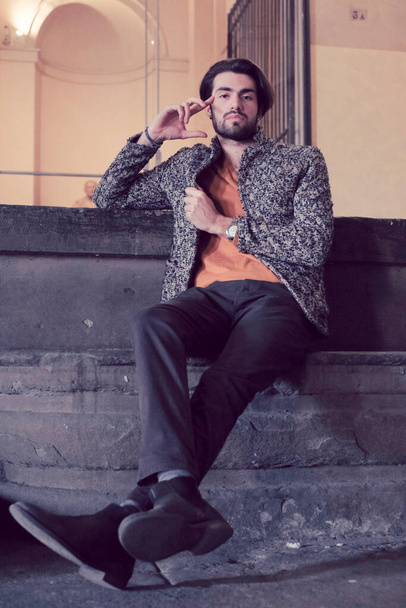 красивый элегантный темноволосый итальянский мальчик в куртке в центре Пармы на ступенях Пилотты. Высокое качество фото - Фото, изображение