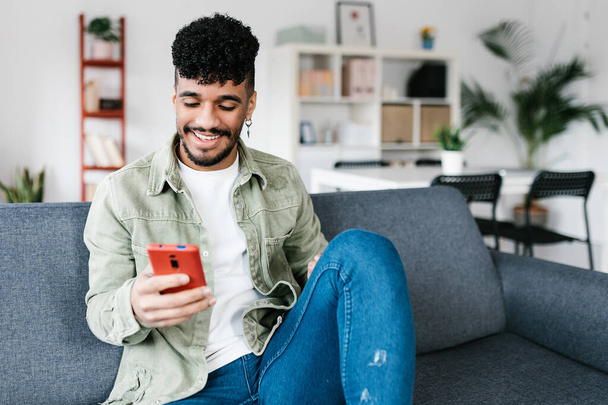 Multiracial man sitting on a couch at the living room and using mobile phone - Photo, Image