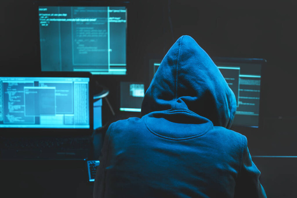 Hacker using computer for organizing massive data breach attack on goverment servers. Hacker in dark room surrounded computers - 写真・画像