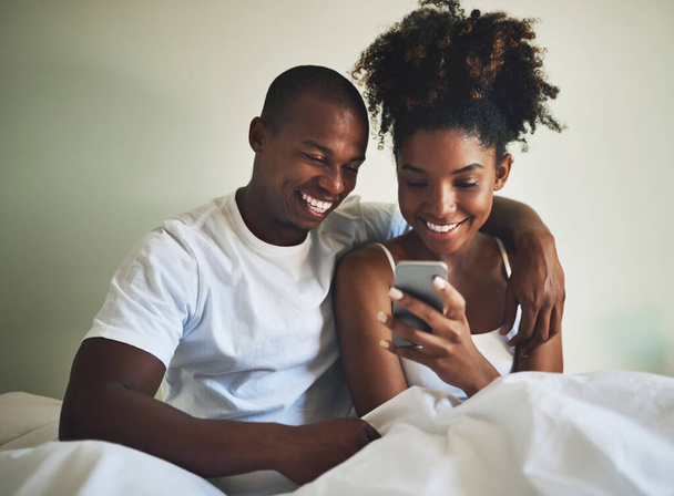 Nic tak nie wyraża miłości jak wspólne konto w mediach społecznościowych. Strzał szczęśliwej młodej pary używającej telefonu komórkowego razem w łóżku w domu. - Zdjęcie, obraz