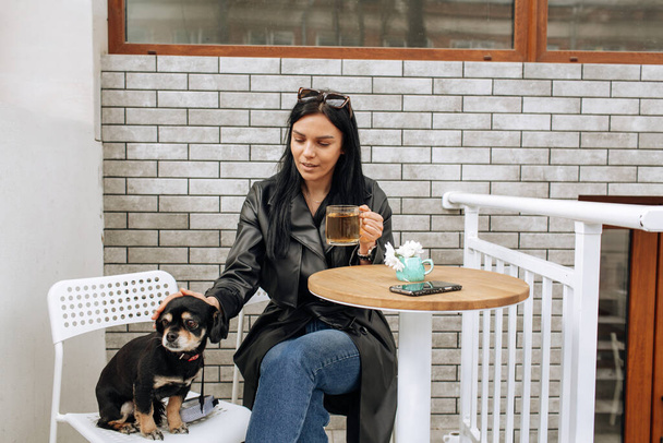 beautiful girl model eats in a cafe on the street with a black dog. hugs, loves. light background. High quality photo - Foto, imagen