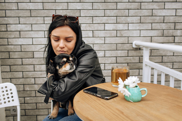 beautiful girl model eats in a cafe on the street with a black dog. hugs, loves. light background. High quality photo - Fotoğraf, Görsel