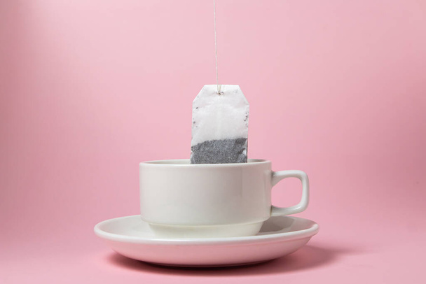 Bolsa de té en una taza blanca sobre un fondo rosa. Una manera rápida y fácil de preparar té. - Foto, imagen