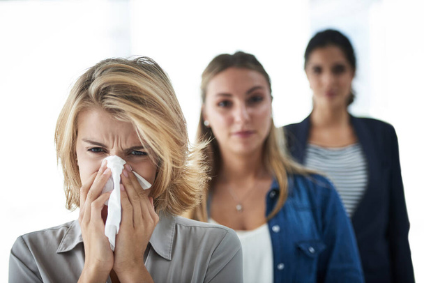 We work even if were sick. Shot of a group of businesswomen standing in a row and looking at the camera with one blowing her nose. - Foto, imagen