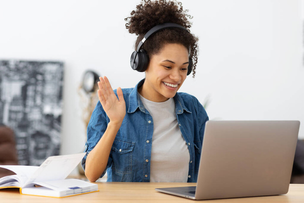 Portrait of happy African American female student in headphones using laptop computer having video call sitting in modern office or home, learning language. Freelancer working remotely, discussion something - Foto, imagen