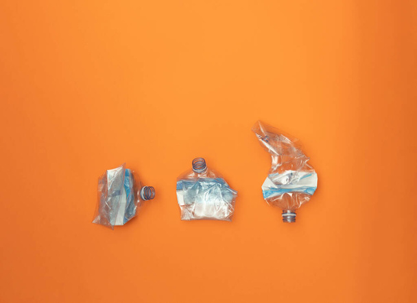 Три измельченные пластиковые бутылки на оранжевом фоне. Концепция использования пластика. Привлекательный экологический плакат. - Фото, изображение