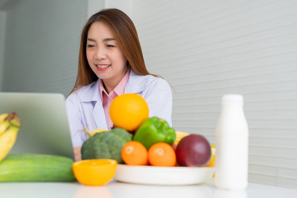Retrato de mujer asiática sonriente nutricionista escribiendo en el ordenador portátil para el plan de dieta correctiva equilibrada para el paciente o consejo de pérdida de peso. Concepto de estilo de vida saludable, comida saludable, dieta - Foto, imagen