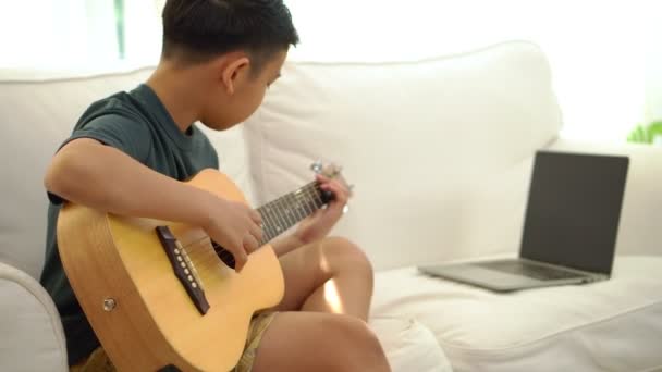 Asiatique garçon apprendre à jouer de la guitare en réunion virtuelle pour jouer de la musique en ligne avec un ami ou un enseignant en vidéoconférence avec ordinateur portable pour en ligne, Communication sur Internet concept d'apprentissage - Séquence, vidéo