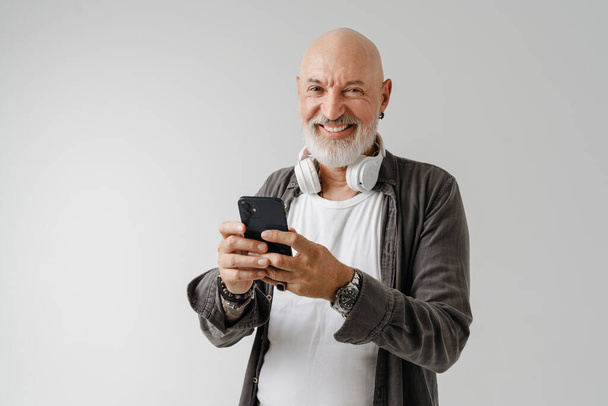Bald european man with headphones using mobile phone isolated over white background - Foto, Imagen