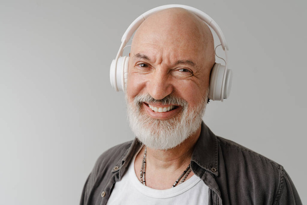 Bald bearded european man listening music with headphones isolated over white background - Foto, Imagen