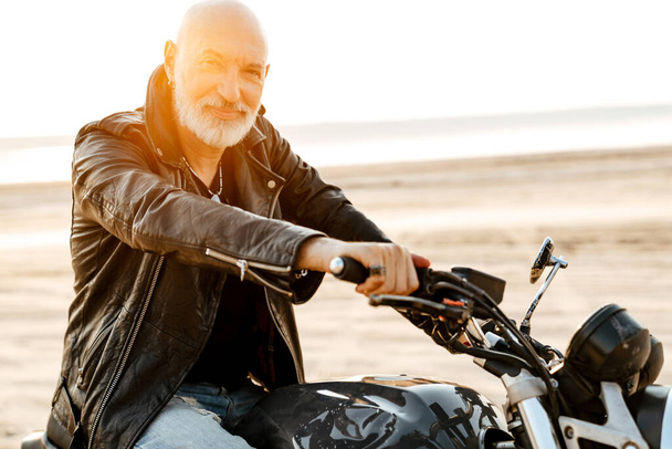 Bold senior man wearing leather jacket riding motorcycle outdoors on summer day - Fotografie, Obrázek