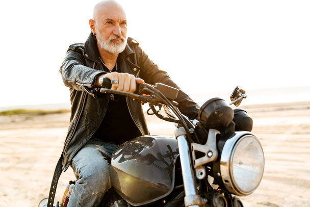 Bold senior man wearing leather jacket riding motorcycle outdoors on summer day - Фото, зображення