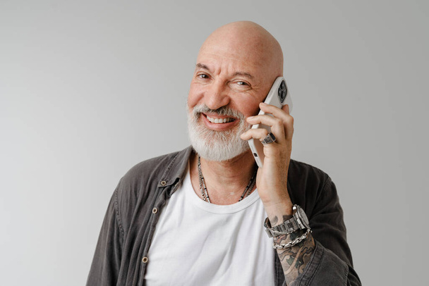 Bald european man with beard talking on using mobile phone isolated over white background - Фото, изображение