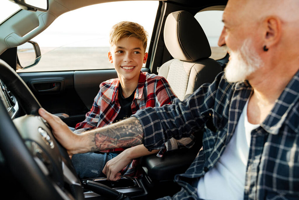 Happy middle aged father and his preschooler son sitting in a car driving father teaching son how to drive - Foto, Imagen