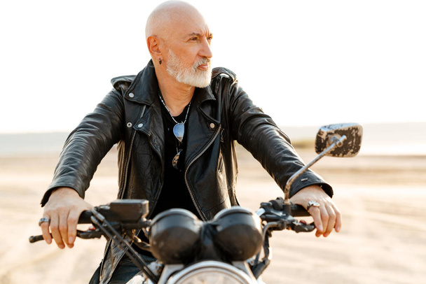 Bold senior man wearing leather jacket riding motorcycle outdoors on summer day - Fotoğraf, Görsel