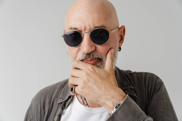 Bald european man in sunglasses holding his chin and looking at camera isolated over white background - Photo, image
